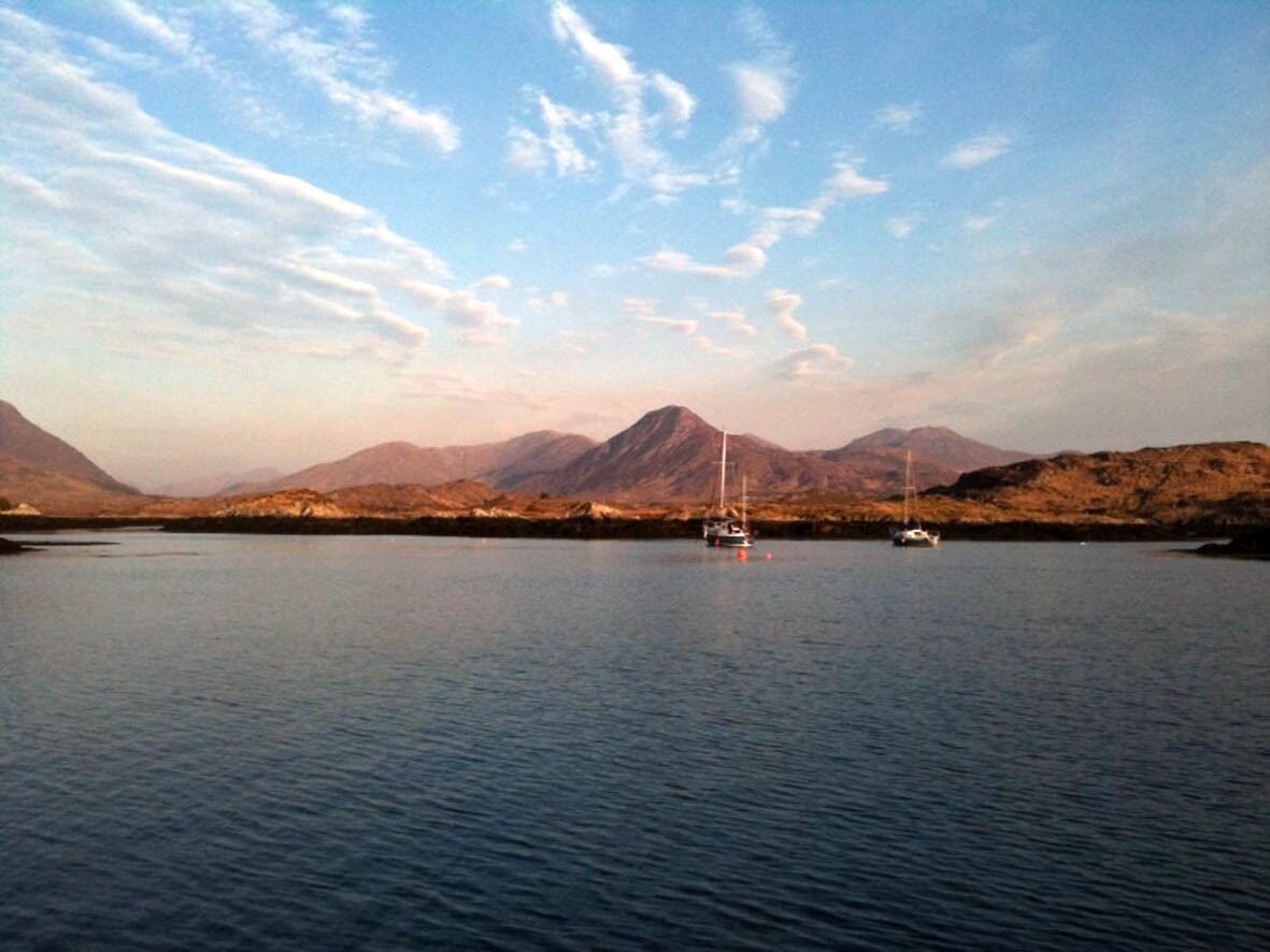 A calm lake with sailboats, surrounded by mountains.