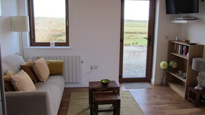 A living room with a sofa, a coffee table, a bookshelf, a TV, and a view through the door. - Atlantic Apartment. Wonderful views of the Wild Atlantic Ocean and mountains (Renvyle)