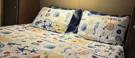 A bed with a quilt featuring sea creatures and the word "BEACH" repeated.