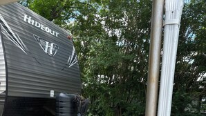 En autocamper med et "Hideout" logo, omgivet af plantekasser og en støbt indkørsel.