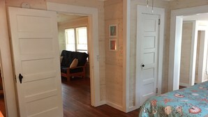 A bedroom with wooden flooring, a bed with a floral bedspread, a door leading to another room, and a window with blinds. - Short walk to beach or Pier Village, We consider FLETC (Saint Simons Island)