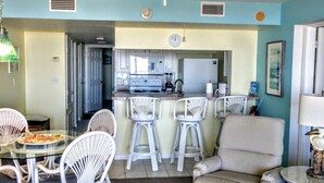 A living room with a dining area, a kitchen in the background, and a ceiling fan. - OCEAN FRONT Classy, Beachy Double Balcony Condo #306 at Cape Winds Resort (Cape Canaveral)