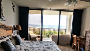 A bedroom with a large bed, a desk, and a view of the ocean. - OCEAN FRONT Classy, Beachy Double Balcony Condo #306 at Cape Winds Resort (Cape Canaveral)