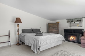A bedroom with a bed, a lamp, a dresser, a fireplace, and a chair.