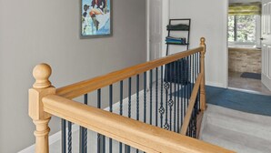 A wooden staircase with a chandelier, a framed magazine on the wall, and a door leading to another room.