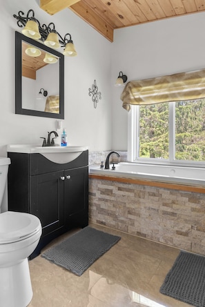 A bathroom with a white toilet, black vanity, and a window with a view of trees.