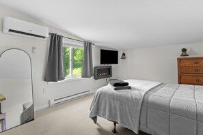 Ein Schlafzimmer mit Bett, Fernseher, Kamin, Kommode und einem Fenster mit Vorhängen.