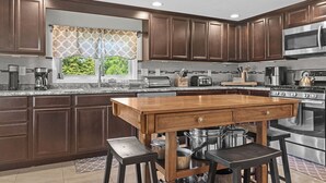 A modern kitchen with dark wood cabinets, stainless steel appliances, a large island with stools, and a window with patterned curtains.