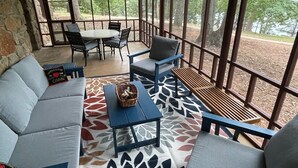 Un espacio de estar techado al aire libre con pared de piedra, una mesa con sillas y vistas a árboles.
