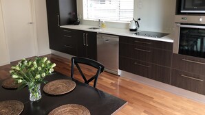 A modern kitchen with dark wood cabinets, a stainless steel dishwasher, and a microwave. There is a window with blinds, a sink, and a vase with flowers on the counter.