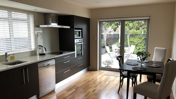 A modern kitchen with dark cabinetry, stainless steel appliances, and a dining area with a table and chairs.