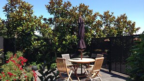 A patio with a round table and two chairs, surrounded by lush greenery and a black fence.