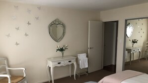 A bedroom with two beds, a vanity with a mirror, a chair, and a door leading to another room.