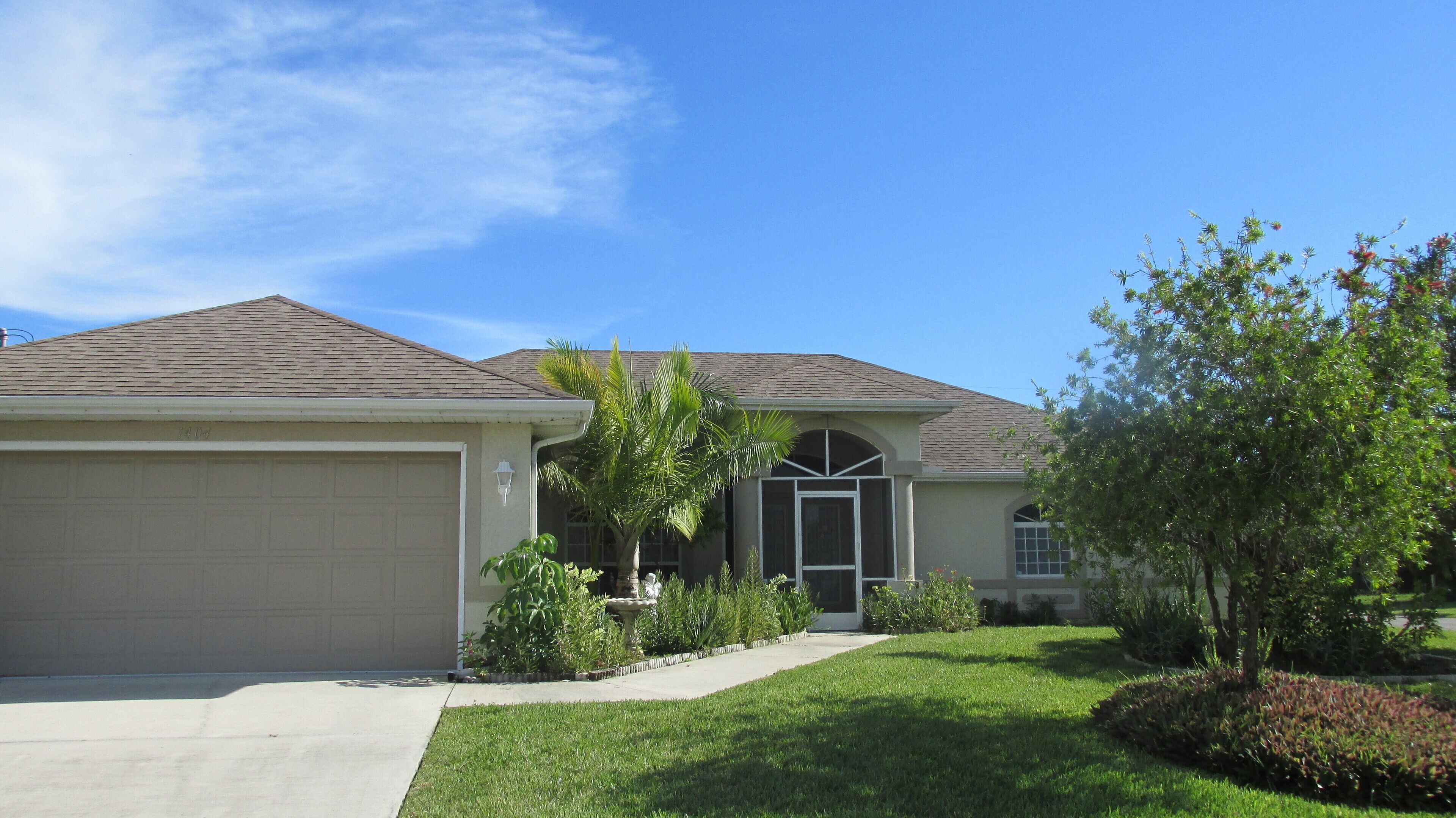 A single-story house with a garage, a front door, and a small garden with various plants and a tree.