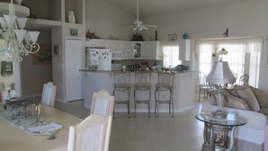 Une cuisine spacieuse dotée d’un îlot central, un coin repas avec une table et des chaises, et un salon avec un canapé et une lampe.