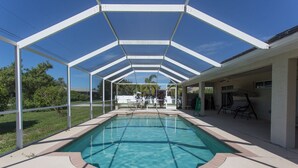 Une piscine couverte avec un bassin à eau cristalline d’un bleu éclatant, entourée d’une structure métallique blanche et bordée de briques.