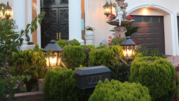 A grand entrance with a large door, white columns, and a well-manicured garden with trimmed bushes and a decorative fountain.