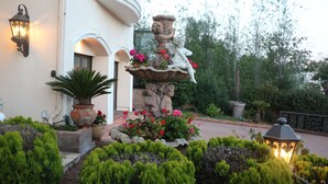 A fountain with a statue of a woman and cherubs, surrounded by well-maintained hedges and potted plants.