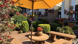 An outdoor patio area with a stone table and chairs, surrounded by potted plants and a large yellow umbrella.