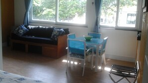 Une pièce confortable avec un canapé, une petite table entourée de chaises et de grandes fenêtres ornées de rideaux.