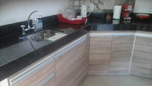 Une cuisine avec un plan de travail noir, des placards en bois, un évier en acier inoxydable et un égouttoir à vaisselle rouge.