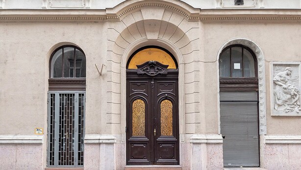 A classical building facade with symmetrical windows, a central arched entrance, and a decorative relief sculpture. - Chic flat by the Great Market Hall (Budapest)