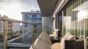 Un balcón con mobiliario de mimbre, barandilla de cristal y vista a la ciudad.