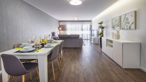 Un comedor moderno con una mesa blanca dispuesta para cuatro, un sofá gris al fondo y una consola blanca con objetos decorativos.