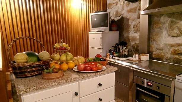 A kitchen with a stone wall, a television on a cabinet, and various fruits and vegetables on the counter. - My Portugal for all Lousada Villa (LOUSADA)