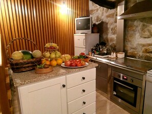 A kitchen with a stone wall, a television on a cabinet, and various fruits and vegetables on the counter. - My Portugal for all Lousada Villa (LOUSADA)