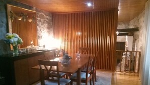 A dining area with a wooden table and chairs, a vase with flowers, and a stone wall. - My Portugal for all Lousada Villa (LOUSADA)
