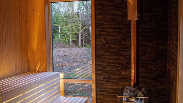 A wooden interior with a bench, a fireplace, and a view of the outdoors. - A 19th century village where you live in the middle of the forest among Deer and Elk. (Perstorp)
