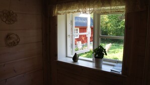 A wooden interior with a window overlooking a red building and greenery. - A 19th century village where you live in the middle of the forest among Deer and Elk. (Perstorp)