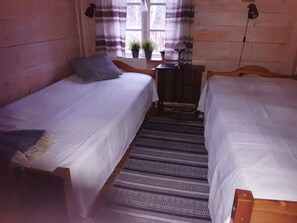 Une chambre avec deux lits simples, une petite table avec une lampe et une fenêtre avec des rideaux.