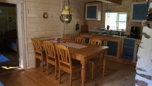 A wooden interior with a dining table, chairs, a hanging light fixture, and a kitchen area with cabinets and a sink. - A 19th century village where you live in the middle of the forest among Deer and Elk. (Perstorp)