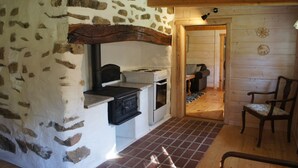 A rustic kitchen with a stone wall, a wooden beam, a stove, and a chair. - A 19th century village where you live in the middle of the forest among Deer and Elk. (Perstorp)