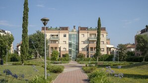 A multi-story residential building with a central glass facade, surrounded by greenery and a paved pathway.