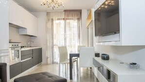 A modern kitchen with a dining area, a TV, and a sofa.