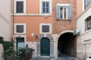 A narrow alleyway with a green door, a small archway, and a building with multiple windows and shutters.