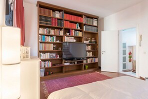 Une chambre à coucher avec une grande bibliothèque, un téléviseur, un lit et une porte donnant sur une autre pièce.
