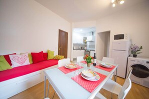A compact living space with a kitchenette, a dining area with a table set for two, and a sofa with colorful cushions.