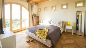Une chambre à coucher avec un grand lit, une commode, un bureau avec un ordinateur, un miroir et une fenêtre donnant sur un beau paysage.