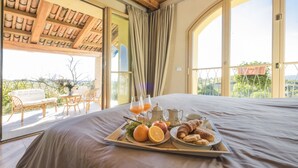 Une chambre avec un grand lit, un plateau de petit-déjeuner comprenant des croissants et des oranges, et une vue sur l’extérieur grâce à de grandes fenêtres.