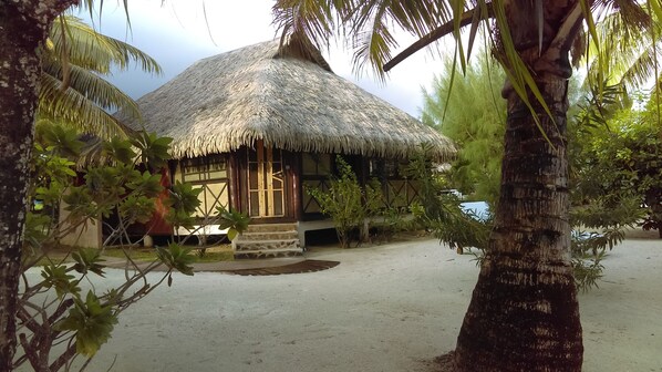 A thatched-roof hut with a wooden door and windows, surrounded by palm trees and a sandy beach. - Fare Pea Iti (Taha'a)