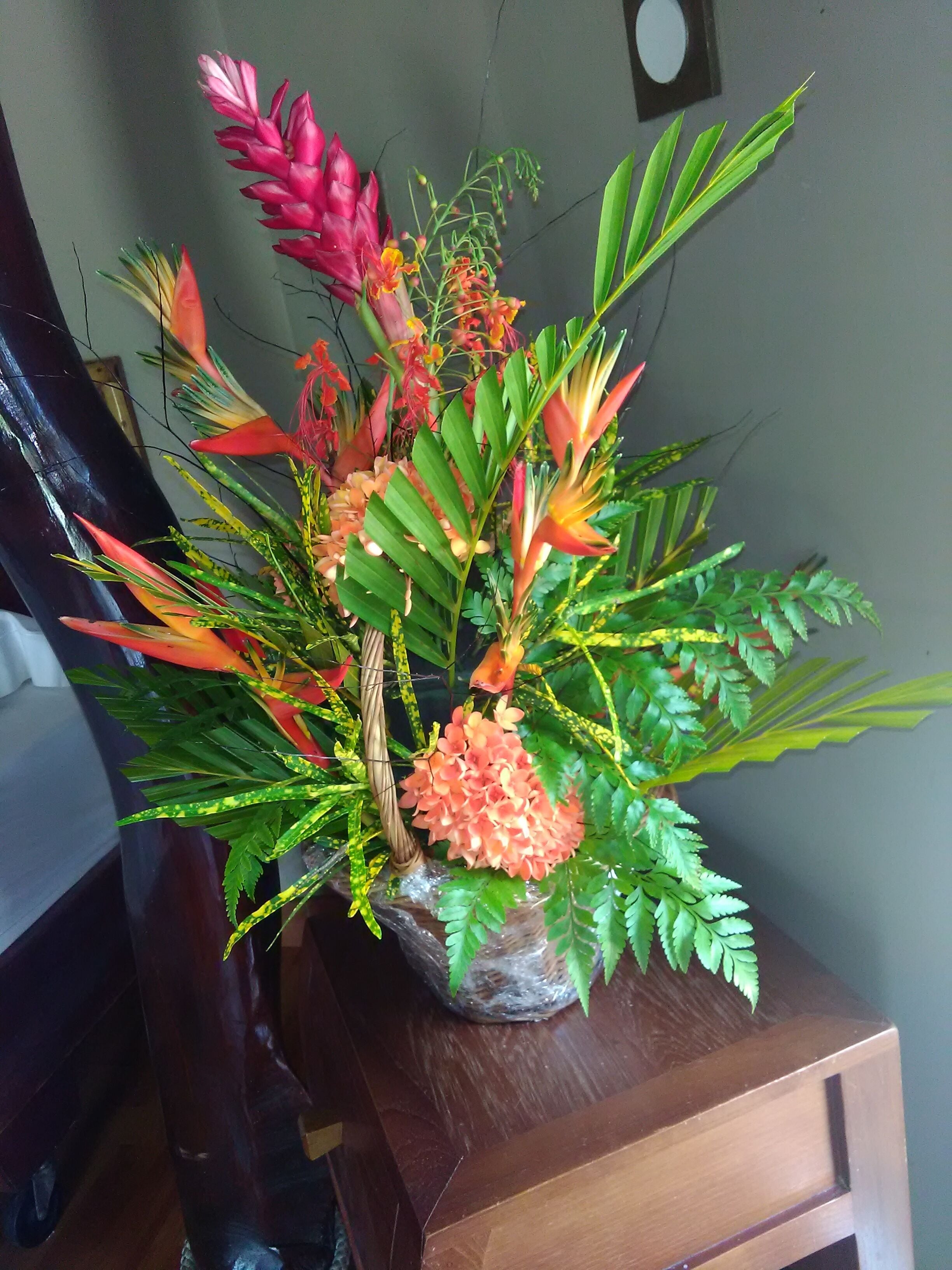 Een houten tafel met een bloemstuk met verschillende tropische planten en bloemen.