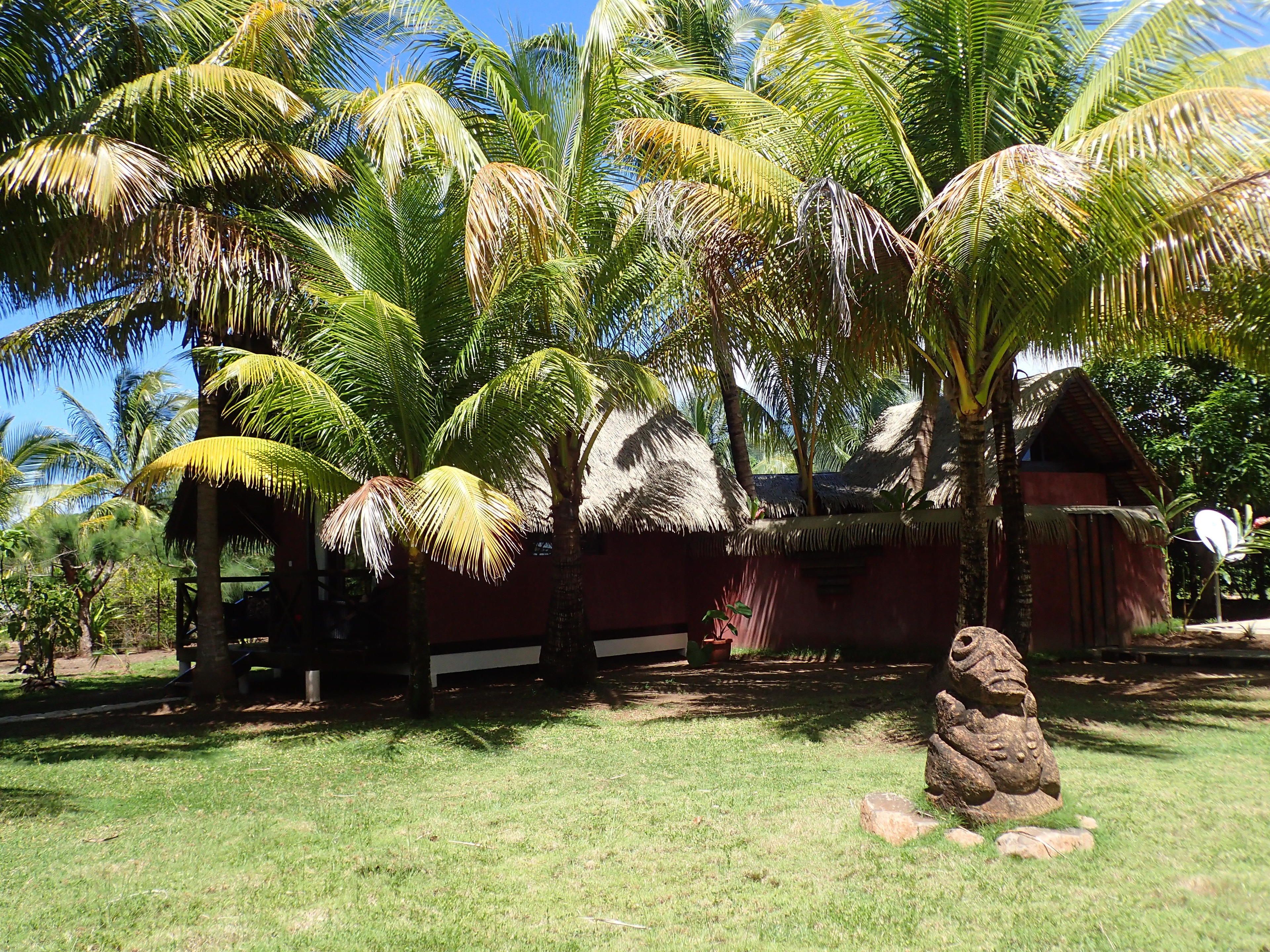 Un entorno tropical con palmeras, una estructura de techo de paja y una escultura de piedra.