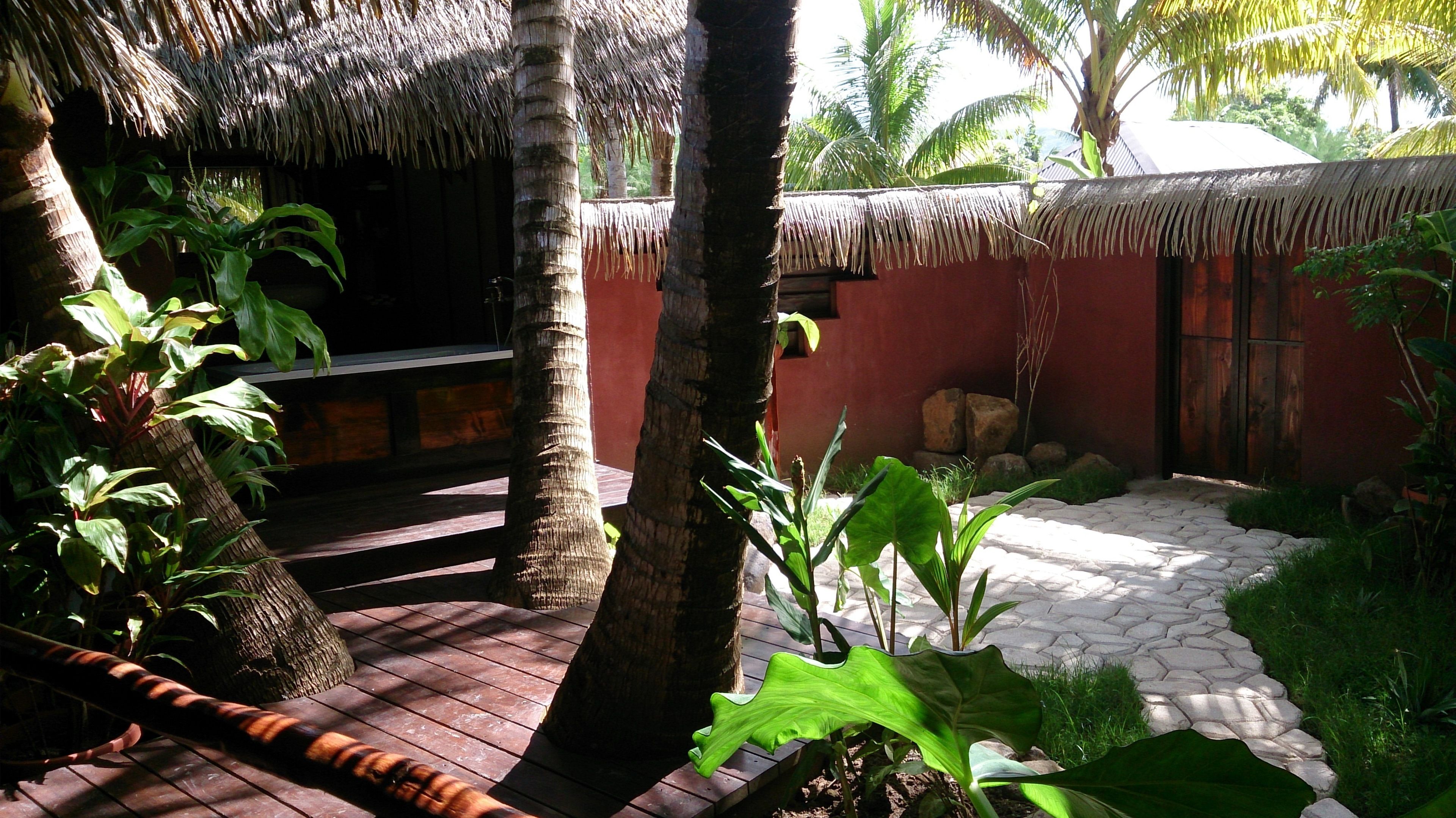 A tropical garden with a thatched-roof structure, palm trees, and a stone pathway.