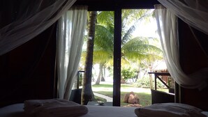 Une chambre à coucher avec un lit, des rideaux blancs et une vue sur des palmiers et un jardin.