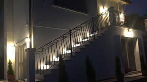 Een modern huis met twee verdiepingen, een trap, potplanten en buitenverlichting.