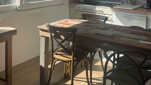 Een keuken met een fornuis, kasten, een raam met uitzicht op bomen en een tafel met stoelen.